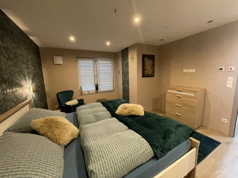 Zweites Schlafzimmer der Ferienwohnung Liesel mit grünem Samtsessel, Kommode und Fenster